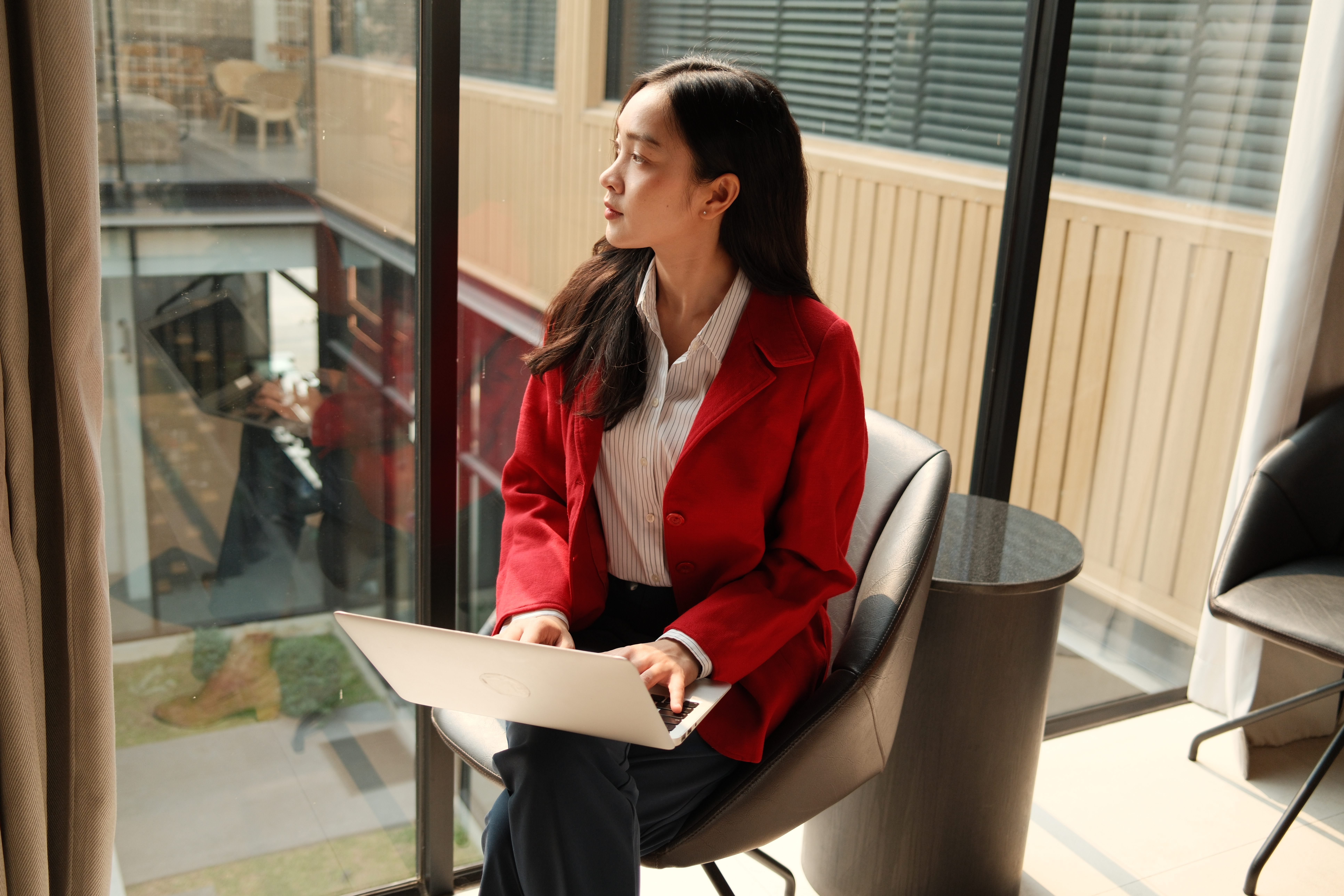 A young female employee sits by a large window, thinking about her career plan.
